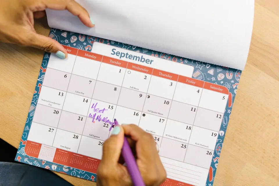 A paper desk calendar with a pen and notes